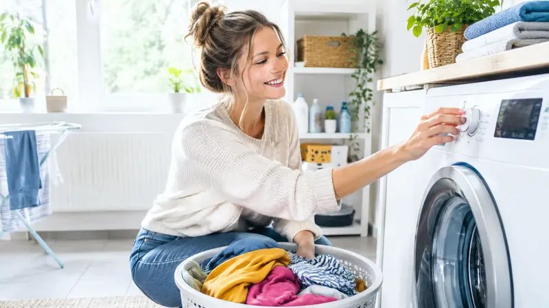 Junge Frau dreht am Programmwahlknopf einer Waschmaschine